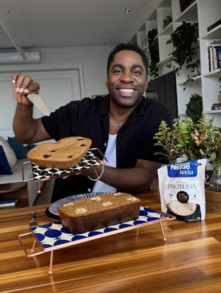 Lázaro Ramos sorrindo com pães caseiros e o pacote de Nestlé Aveia Proteína