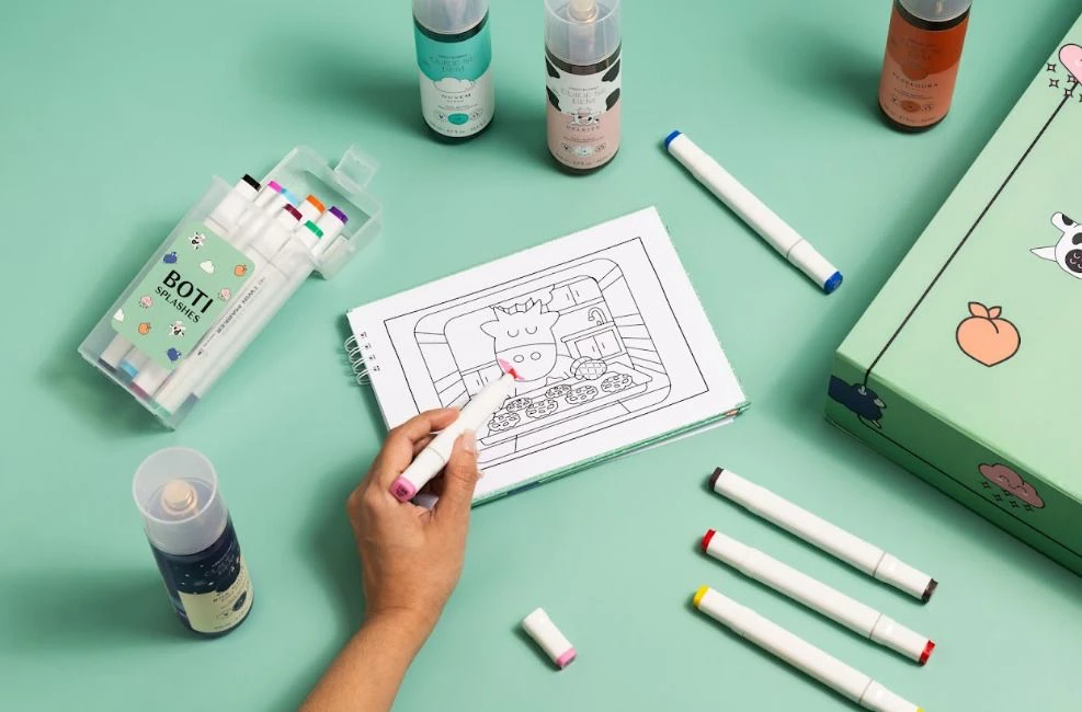 Kit Boti Splashs com livro de colorir, canetas e body splashs sobre fundo verde