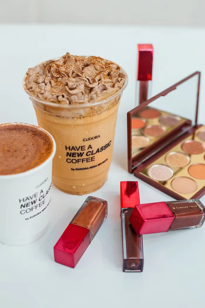 Copos do café Have a New Classic Coffee da Eudora com Niina Secrets ao lado de maquiagens